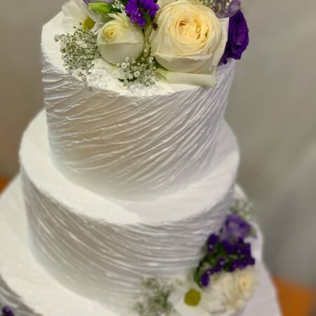 На фотографии свадебный белый торт в три яруса, украшенный цветами, производителя кондитерских изделий на заказ Шарлотка.