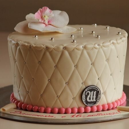На фото круглый торт кремового цвета украшенный бусинами и цветком, производителя кондитерских изделий на заказ Шарлотка.