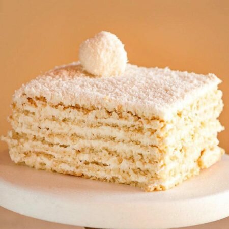 На фотографии торт Рафаэлло, производителя Шарлотка, песочные коржи с белым кремом и посыпанные кокосовой стружкой.